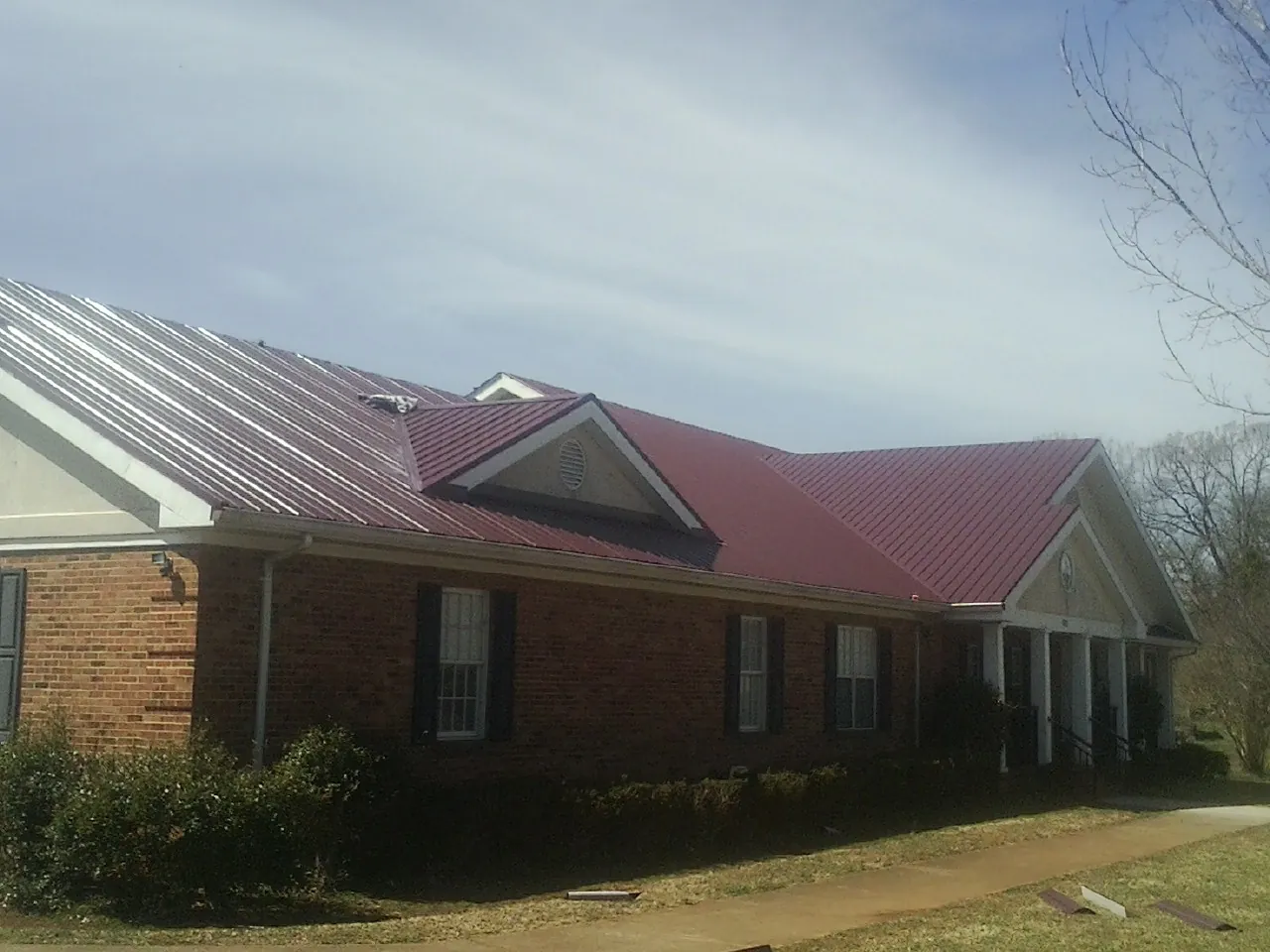 Red metal roof with gabled entries on a long brick building, from a Hail Damage Roof Repair job in Moulton