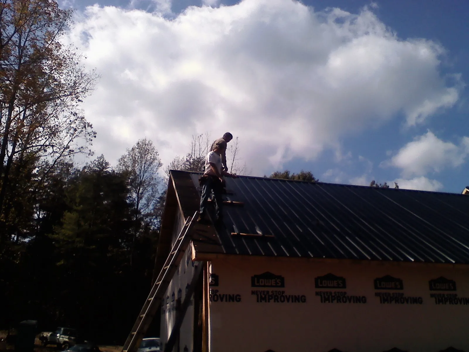 Roofer fastening dark metal panels high against a cloudy sky, from a Roof Inspection job in Moulton