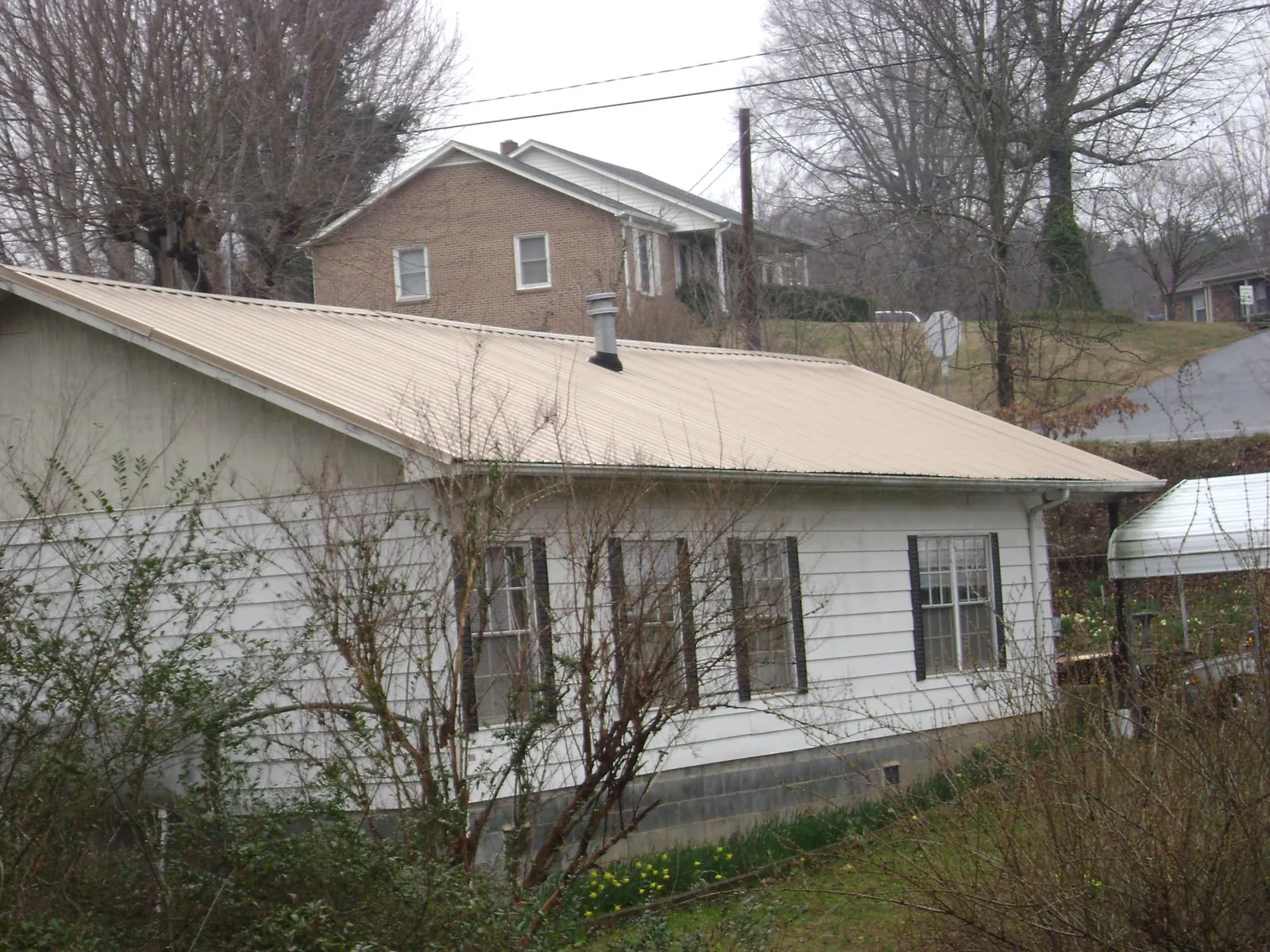 Tan metal roof on a white sided house set into a hillside — Commercial Roofing by Roofing Brothers in Moulton
